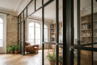 Verrière industrielle en acier noir séparant un salon et un bureau dans un appartement haussmannien rénové avec parquet ancien