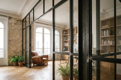Verrière industrielle en acier noir séparant un salon et un bureau dans un appartement haussmannien rénové avec parquet ancien